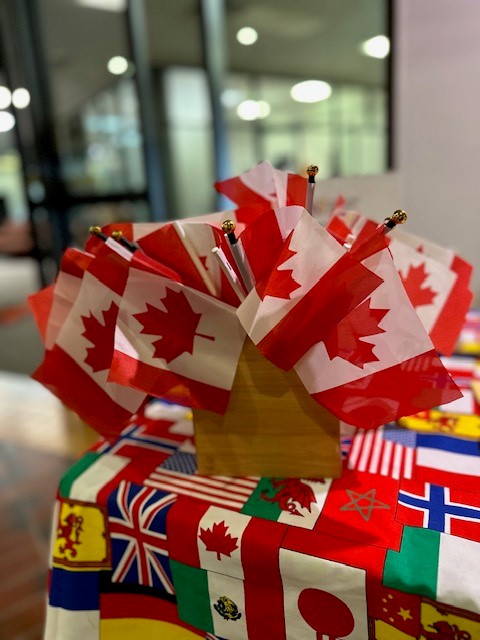 table with a multi flag table cloth and a container holding several small Canadian flags