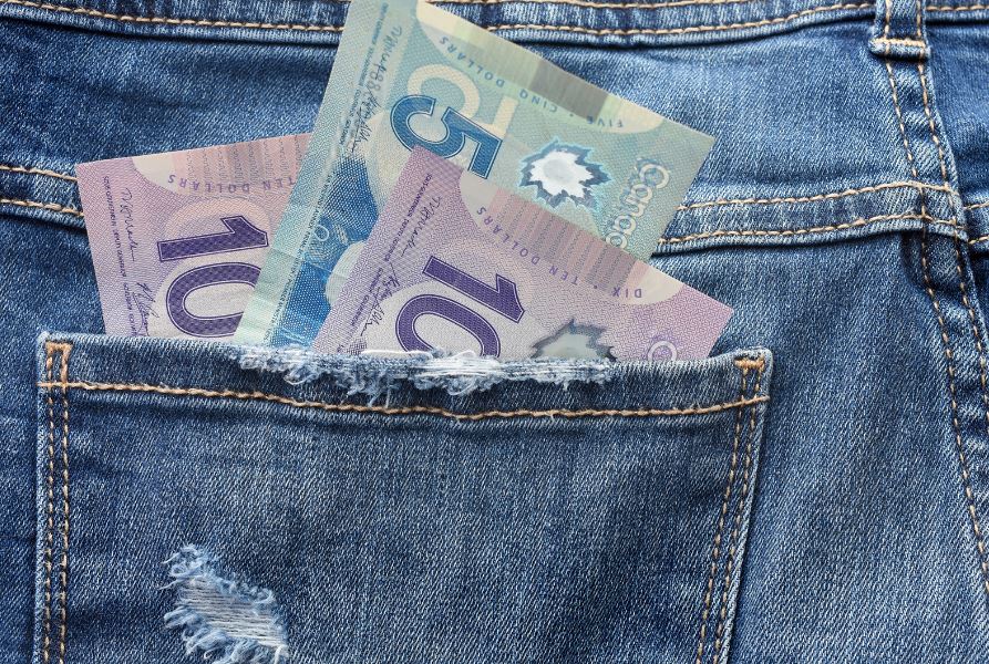bakc pocket of a pair of jeans with Canadian 5 and 10 dollar bills sticking out of the pocket