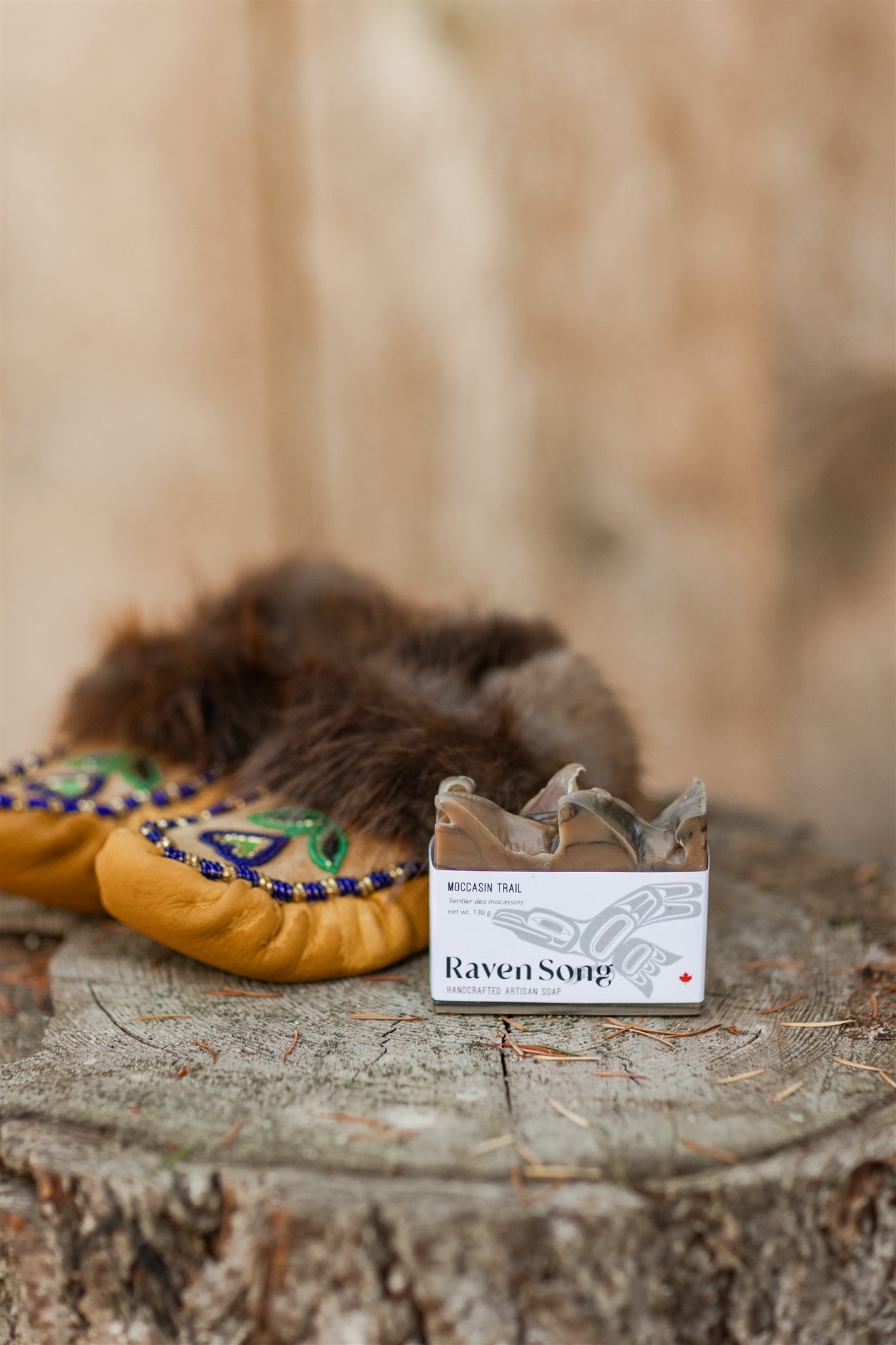 A pair of child's moccasins with Raven Song soap beside them and beautifully displayed on a tree stump