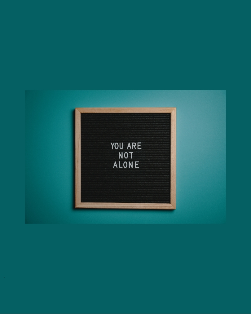 Emerald green background, foreground has sign that reads " you are not alone"