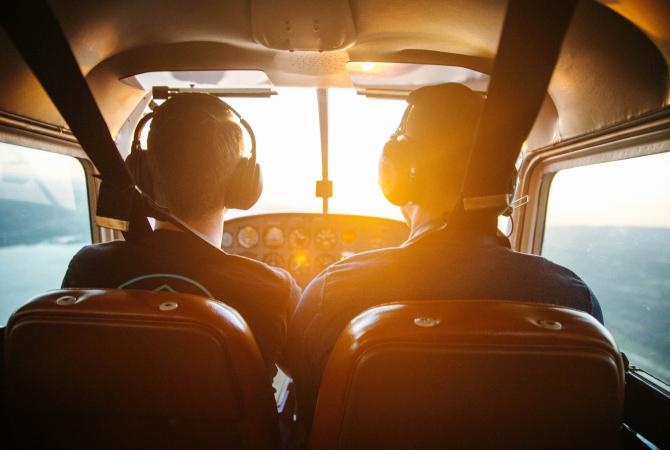 two men flying a small airplane. sun beaming into the cockpit