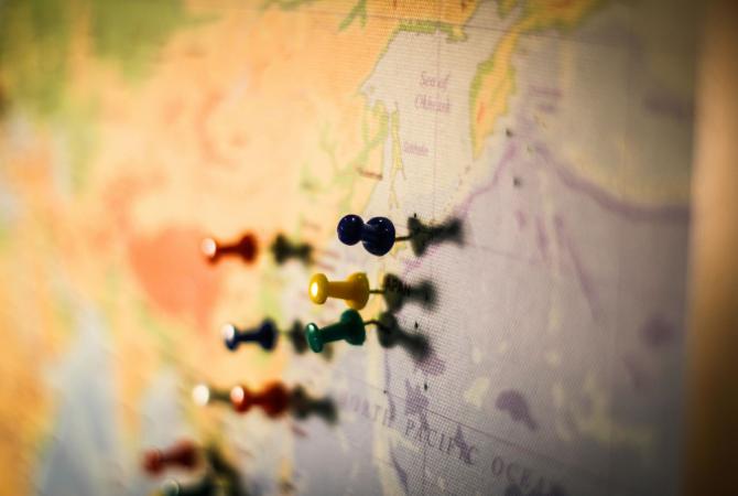 slightly blurred image of a portion of a world map with multi coloured push pins marking different locations