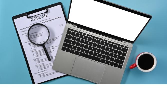 laptop with a resume sitting beside it on one side, and a cup of coffee on the other